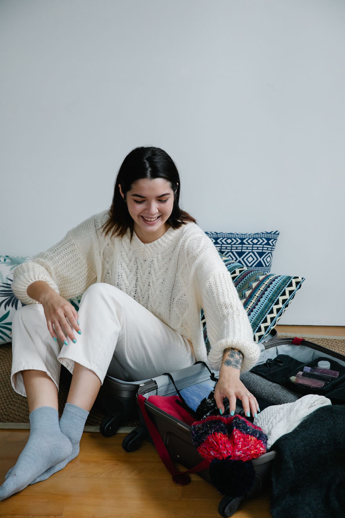 Smiling woman sitting in suitcase packing clothes for travel using vacuum compression bags